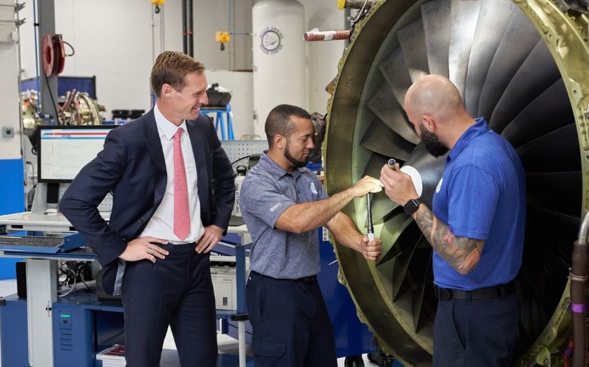 WLFC CEO, Austin Willis, and two team members review a jet engine inside a repair shop. Willis provides innovative and customized aviation services.